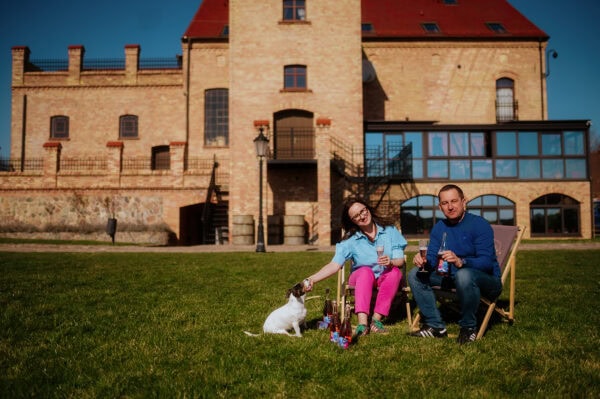 Evoto Para osób z psem na trawie przed zamkiem, wino polskie z lubuskich winnic.